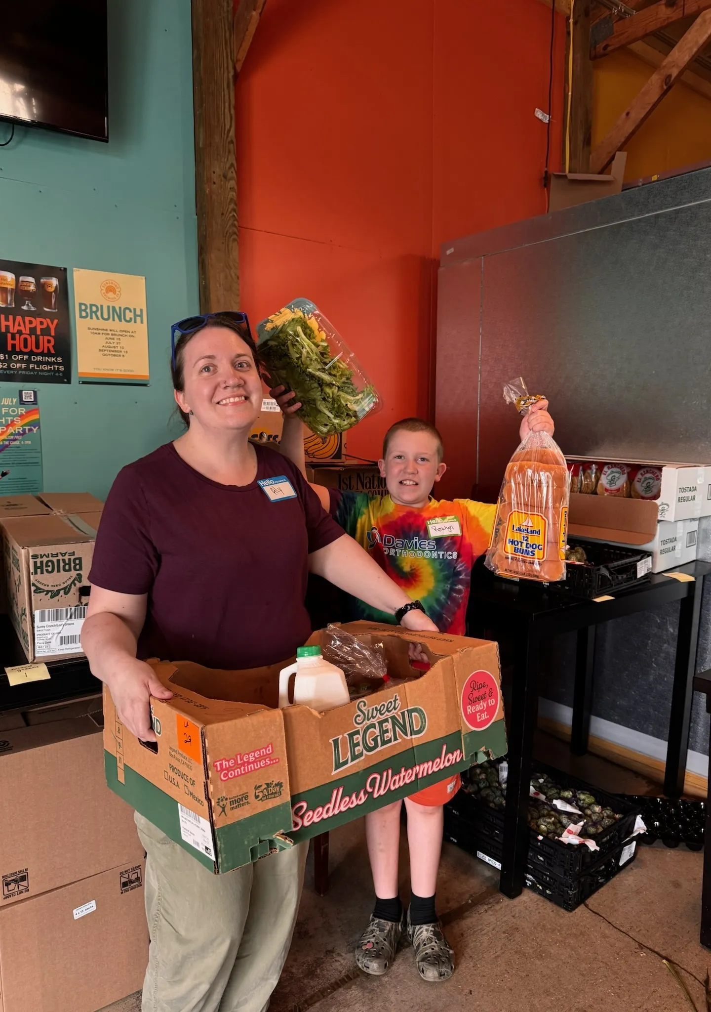 A Sunrise Reach volunteer and a young helper carrying a box of groceries at the monthly pantry