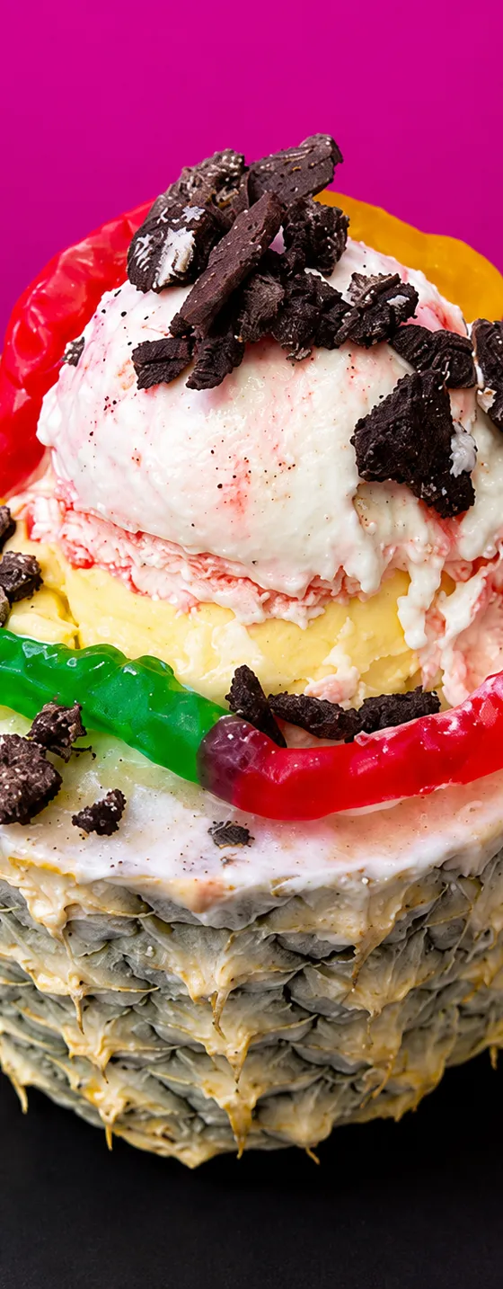 A hollowed pineapple filled with scoops of ice cream, gummy worms, and crushed cookies