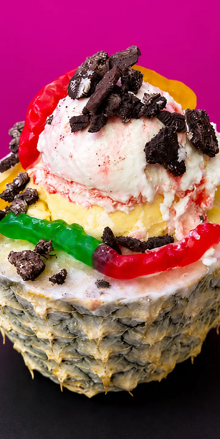 A hollowed pineapple filled with scoops of ice cream, gummy worms, and crushed cookies