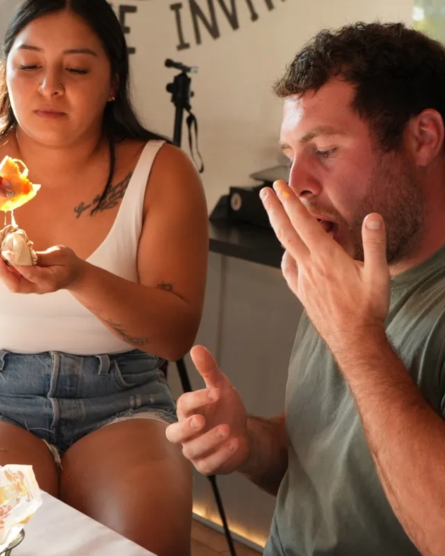 A woman holding a taco and a man beside her at the counter, baskets of food in front of them