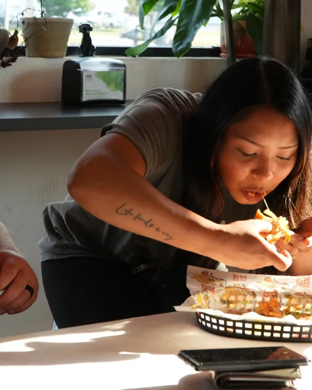 A woman at a table by the window picking food out of a basket lined with Speedy Tacos paper