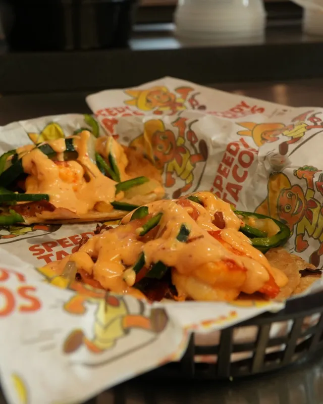 A basket of tacos on Speedy Tacos paper, topped with crema and cilantro