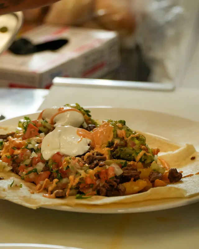 A finished plate of nachos with sour cream and pico de gallo on the counter
