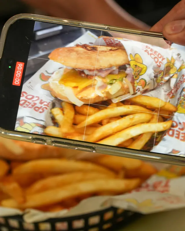 Someone photographing a basket of burger and fries with their phone