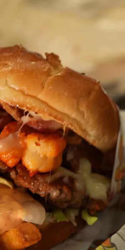 The Surf and turf burger held in Speedy Tacos paper, shrimp and bacon layered over the patty