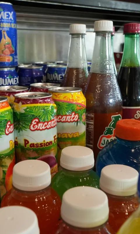 A shelf of Mexican soda bottles and juice cans seen along the row